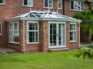 Beautiful brick house features a modern glass conservatory with white trim, overlooking a green lawn.